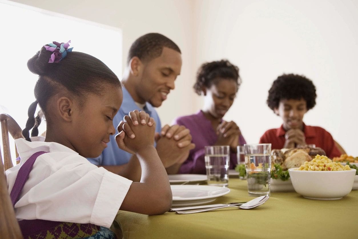 A group of people sitting at the table praying.